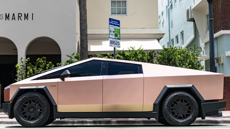 Pink Cybertruck in profile in front of shops