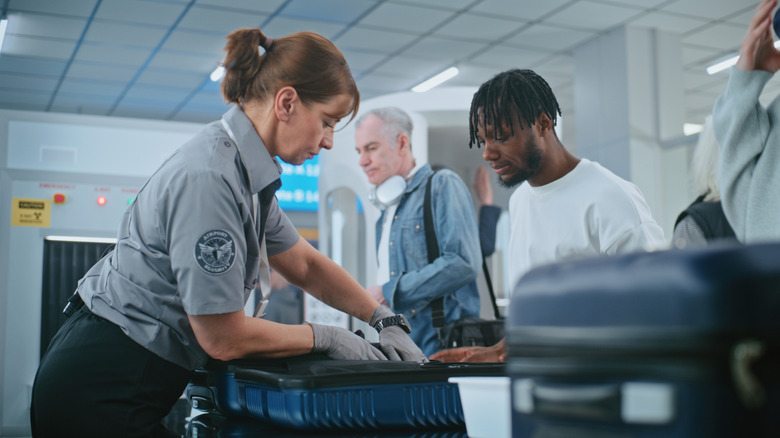 person getting their bag checked at TSA airport checkpoint