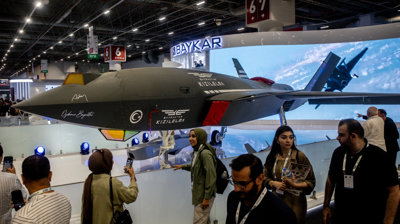 People pose in front of the Baykar, Bayraktar Kizilelma drone on display indoors
