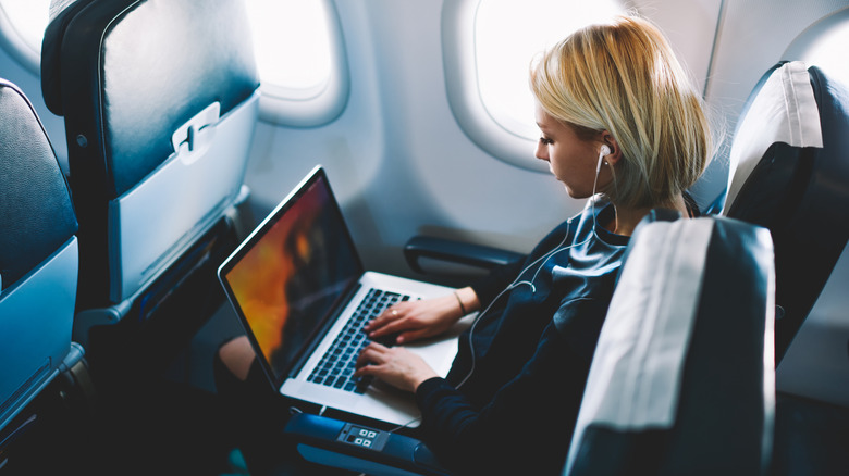A blonde woman using a laptop in-flight.