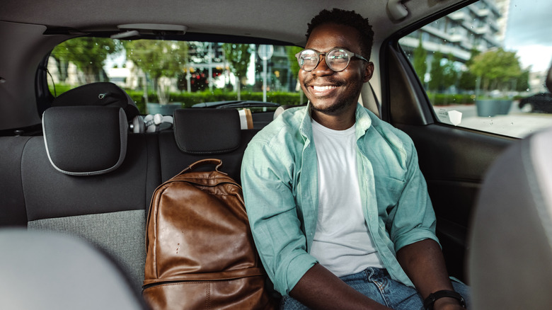 A person smiling in the back seat of a vehicle.