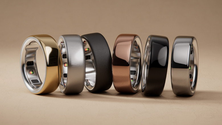 Six Oura smart rings, in the six available colors standing on their edge on a beige surface next to one another.