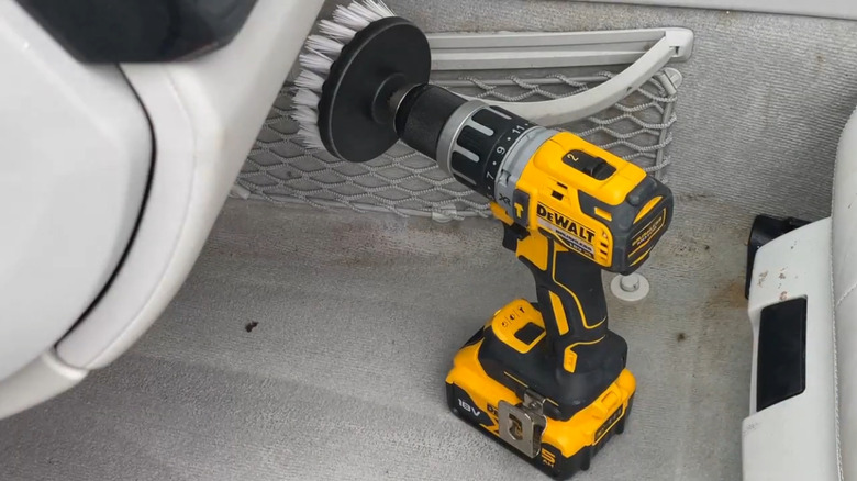 A yellow DeWalt cordless drill fitted with a white scrubbing brush attachment, set on the carpeted floor of a vehicle.