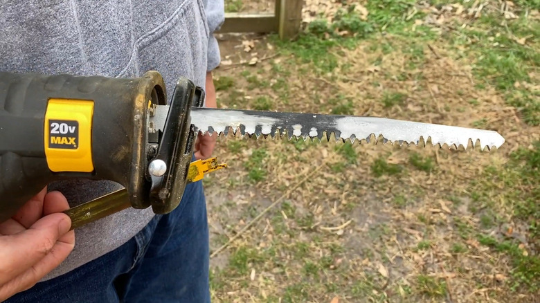 A person holding a DeWalt 20V MAX reciprocating saw with a pruning blade.