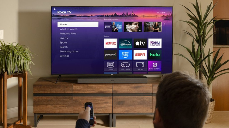 A person holding remote pointing at Roku TV in living room