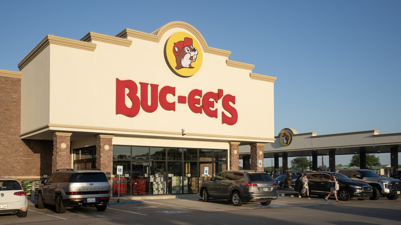 The exterior of a Buc-ee's with gas pumps in the background and cars and people in front.