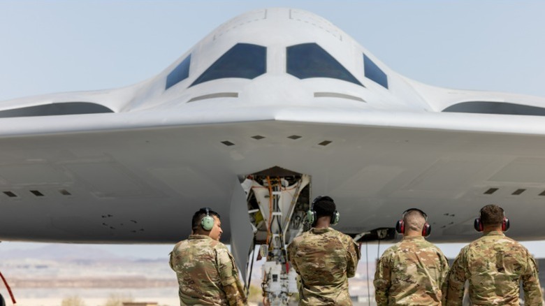 Frontal view of a B-21 bomber parked on the runway with soldiers standing in front of it