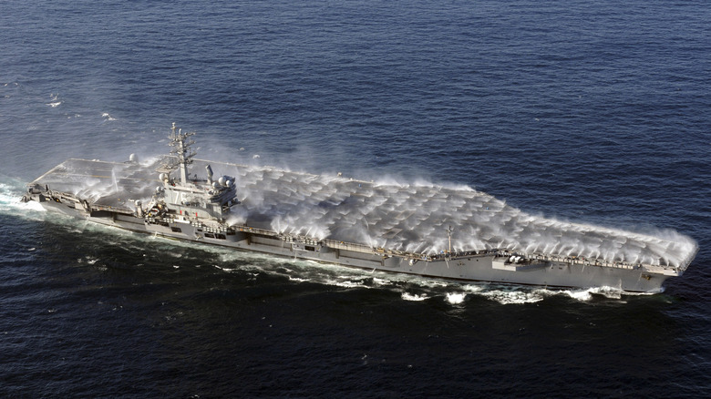 An aircraft carrier at sea with its flight deck sprinkler system deployed