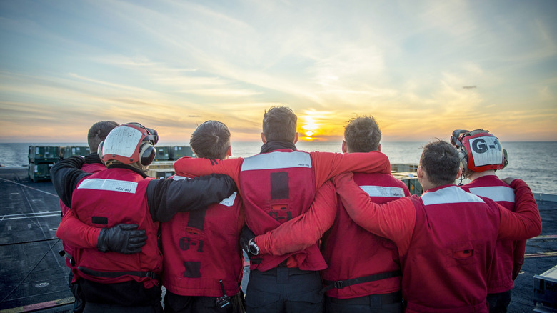 Red jersey crew huddles in front of sunset on an aircraft carrier flight deck