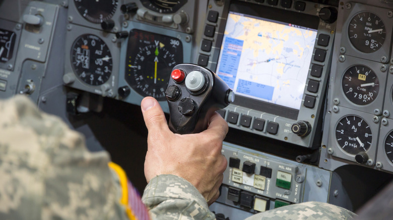 U.S. soldier's hand rests on control stick with red pickle button centered in a military jet simulator