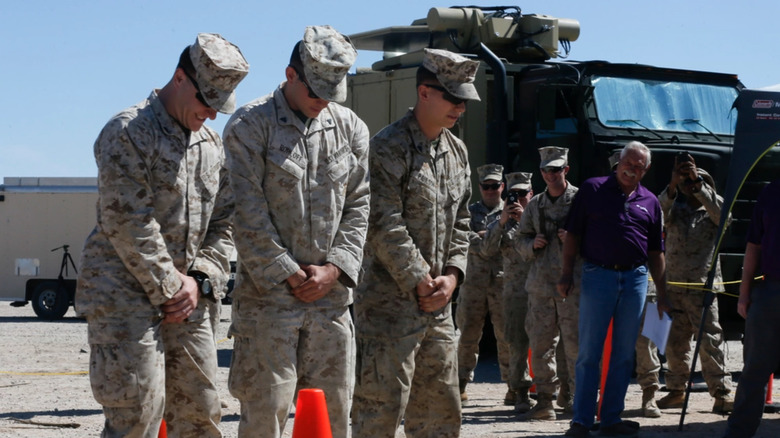 Three soldiers participating in an Active Denial System test with onlookers in the background