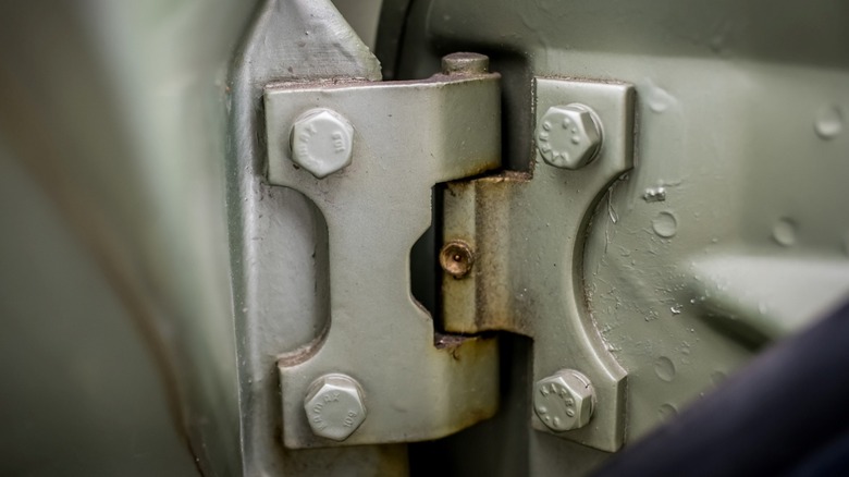 rusty door hinge on grey car viewed from inside of open door