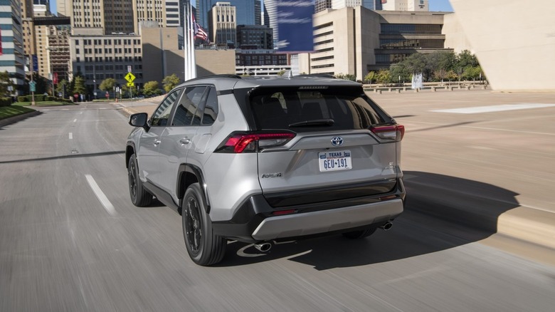 A rear three-quarter view of a silver 2022 Toyota RAV4 hybrid driving through city streets.