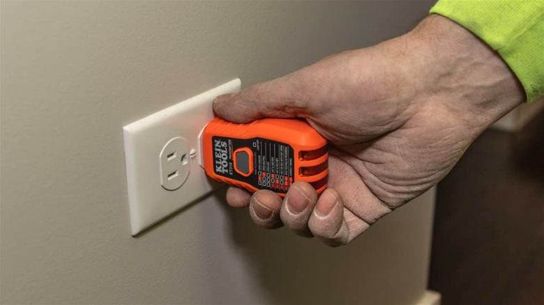 A hand plugging a GFCI Outlet Tester in a power outlet.