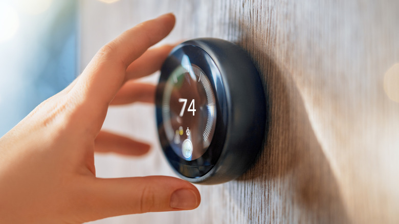A person reaching for a smart thermostat stuck on a wall