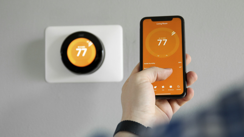 A person adjusting a thermostat with a phone.