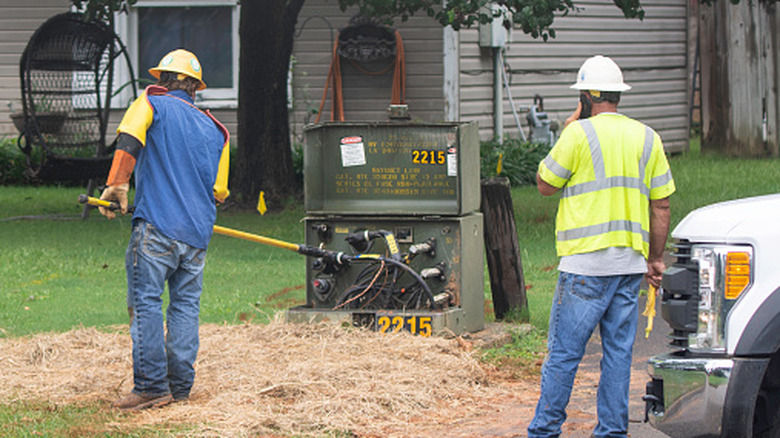 Two electric company linemen working on a power transformer in a suburban neighborhood.