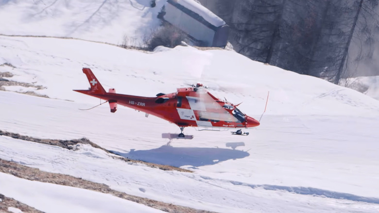 Rega Da Vinci helicopter hovering over a snowy mountain surface