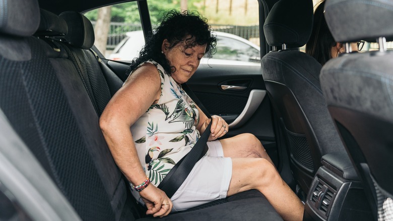 Woman fastening a rear seatbelt inside a car viewed from right side