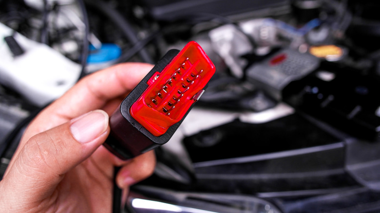 A hand holding a red OBD2 diagnostic connector plug up