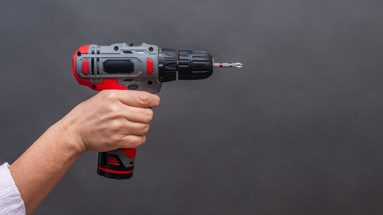 A person holding a black, gray, and red cordless power drill against a gray background