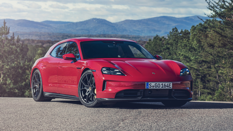 A red Porsche Taycan parked on asphalt with trees and mountains in the background