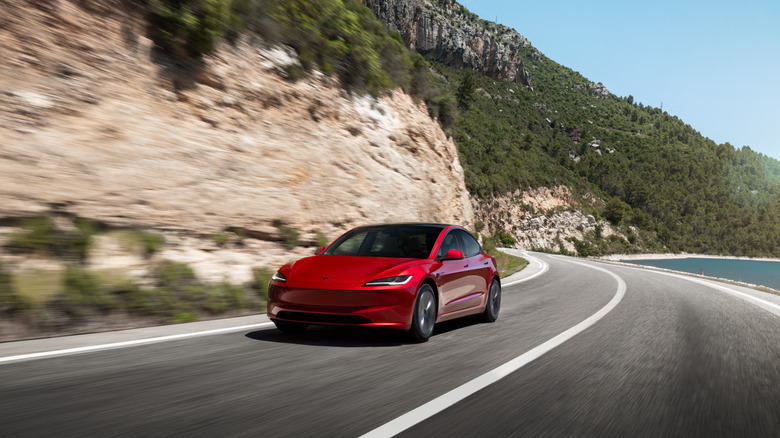 A red Tesla Model 3 on a coastal road