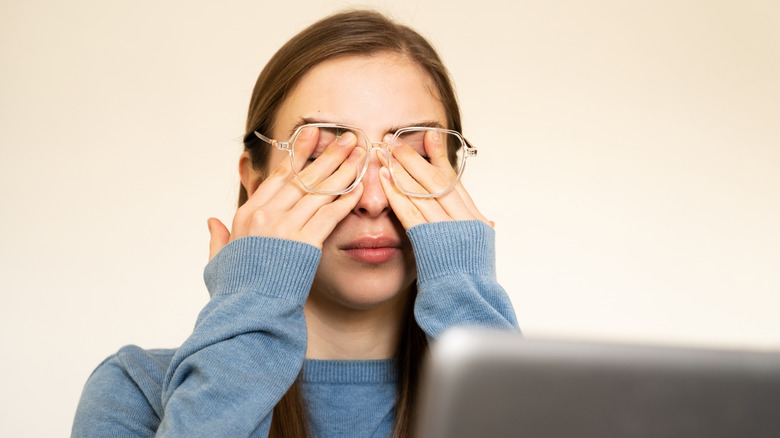 Person with hands over eyes in front of a laptop.