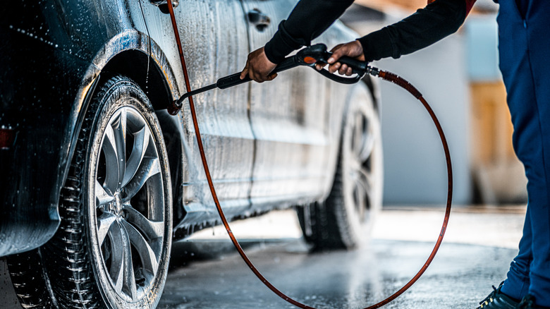 Person washing car rear-right wheel arch with power washer