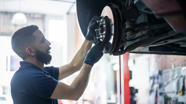 A mechanic holding a car's wheel assembly with the brake calliper.