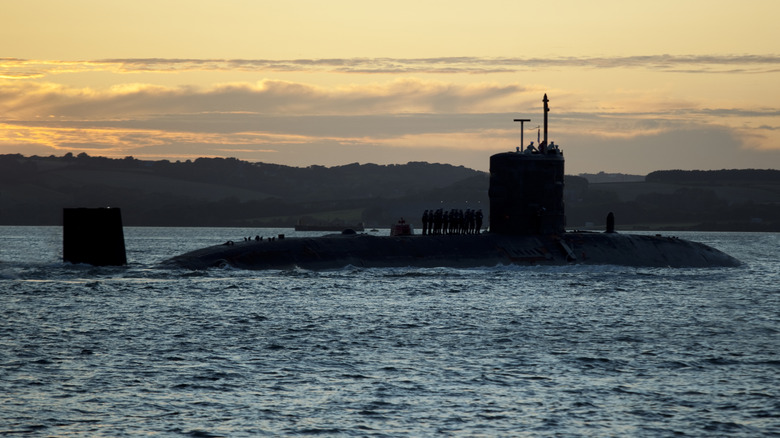 A surfaced submarine with crew standing on hull and a falling sun in the background.
