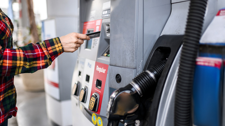 A woman in a flannel shirt making a credit card payment at a gas pump