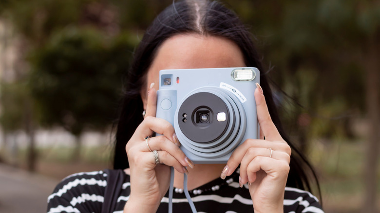 A person holding a newer Polaroid camera in front of their face