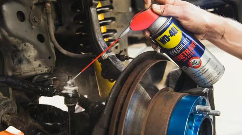 Spraying WD-40 penetrant onto rusty car part
