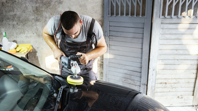 Man using machine polisher on hood of car