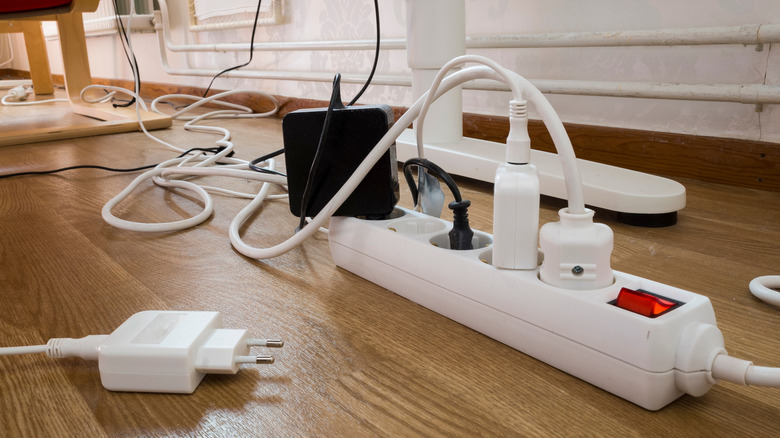 A clutter of cords on a wood floor with a power strip