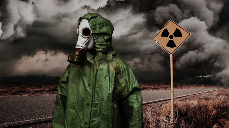 A soldier with a hazmat mask standing in a war zone. 