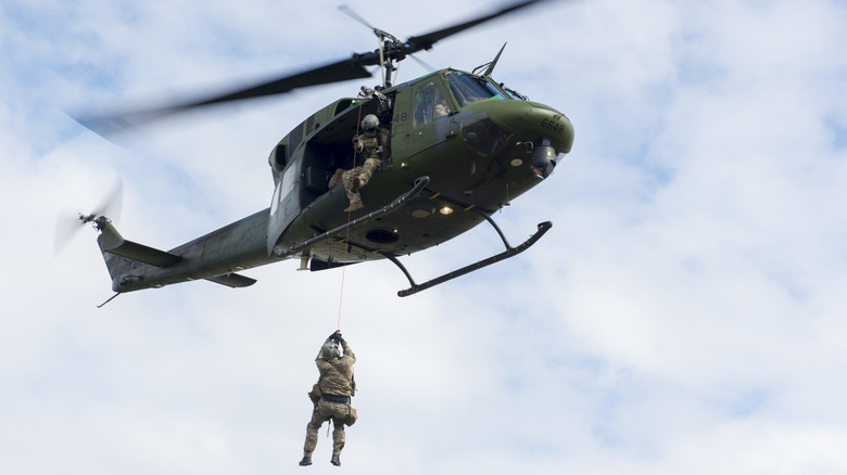 Soldier dangles from rope out of UH-1 Huey helicopter in sky