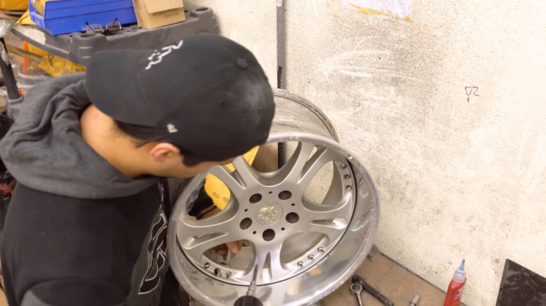 A person working on a three-piece alloy wheel from an unknown brand