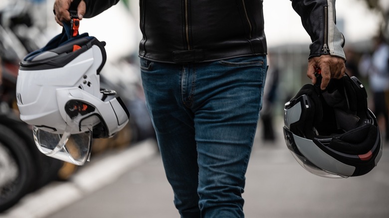 A man carrying two motorcycle helmets.