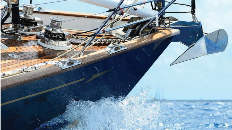 A stainless steel claw anchor mounted to the front of a ship cutting through the water