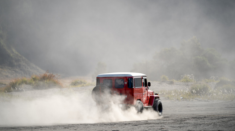 A red FJ40 Toyota Land Cruiser kicking up some dust, rear 3/4 view
