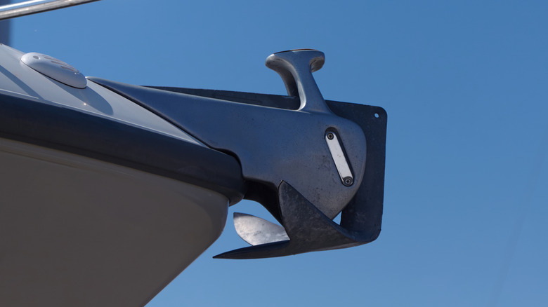 A close-up of a yacht's plow anchor attached to the bow, with a bright blue sky in the background
