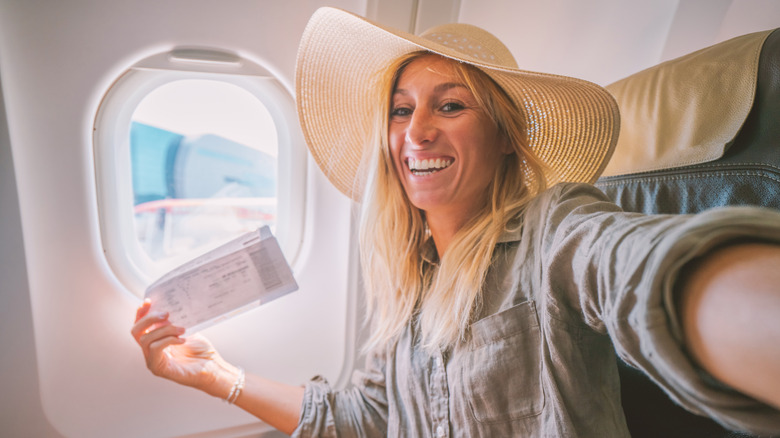 Woman on airplane smiling with boarding passes in her hands