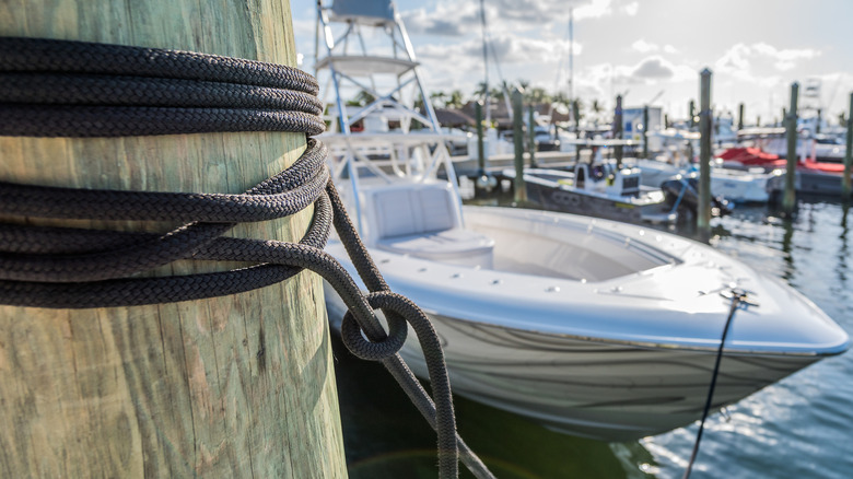 A close-up of a bow line tied around a pier pillar and attached to the bow cleat on a boat in marina