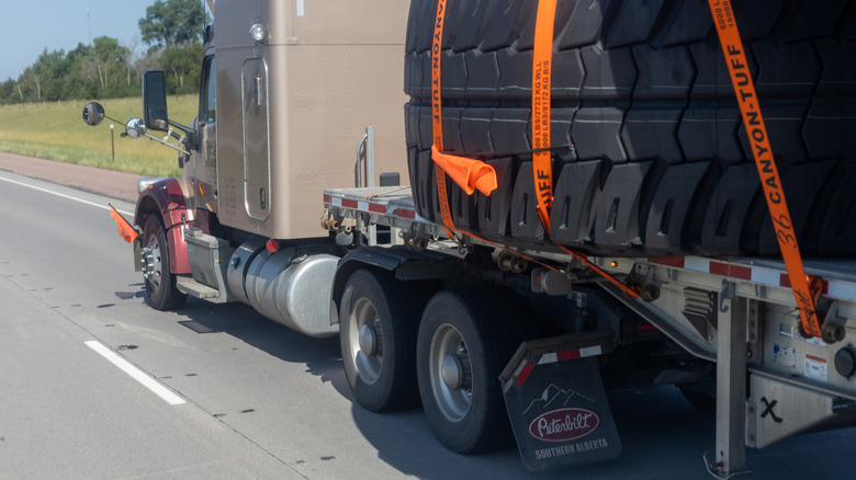 rear left view of Peterbilt tractor with open trailer hauling giant tires