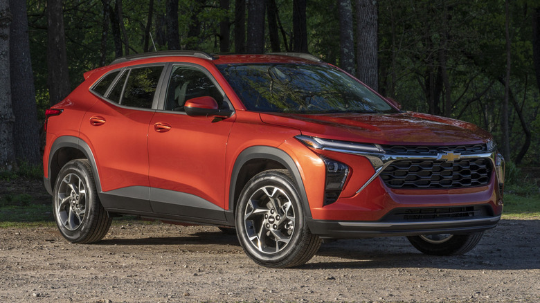Red 2024 Chevrolet Trax parked on dirt in front of a forest