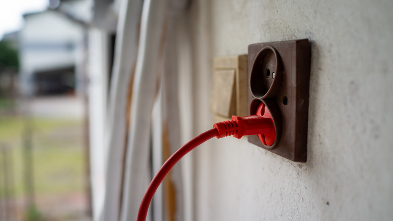 A red extension cord plugged into an outdoor outlet.