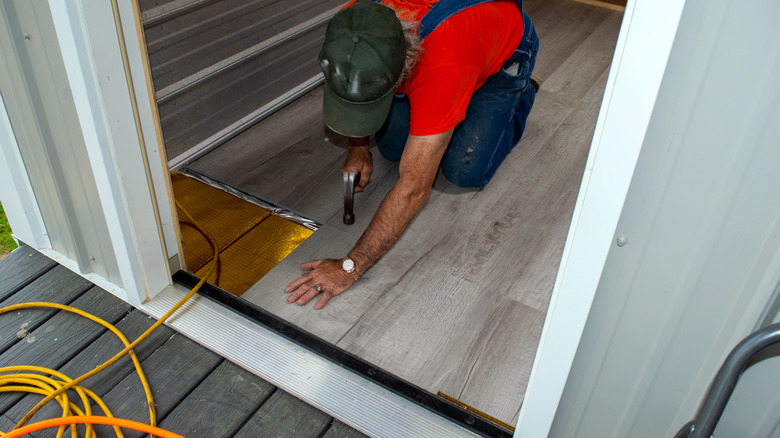 A worker working on a floor near an extension cord snaking through a doorway.