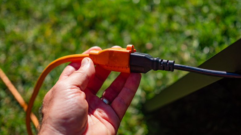 Hand holds orange extension cord connected above grass